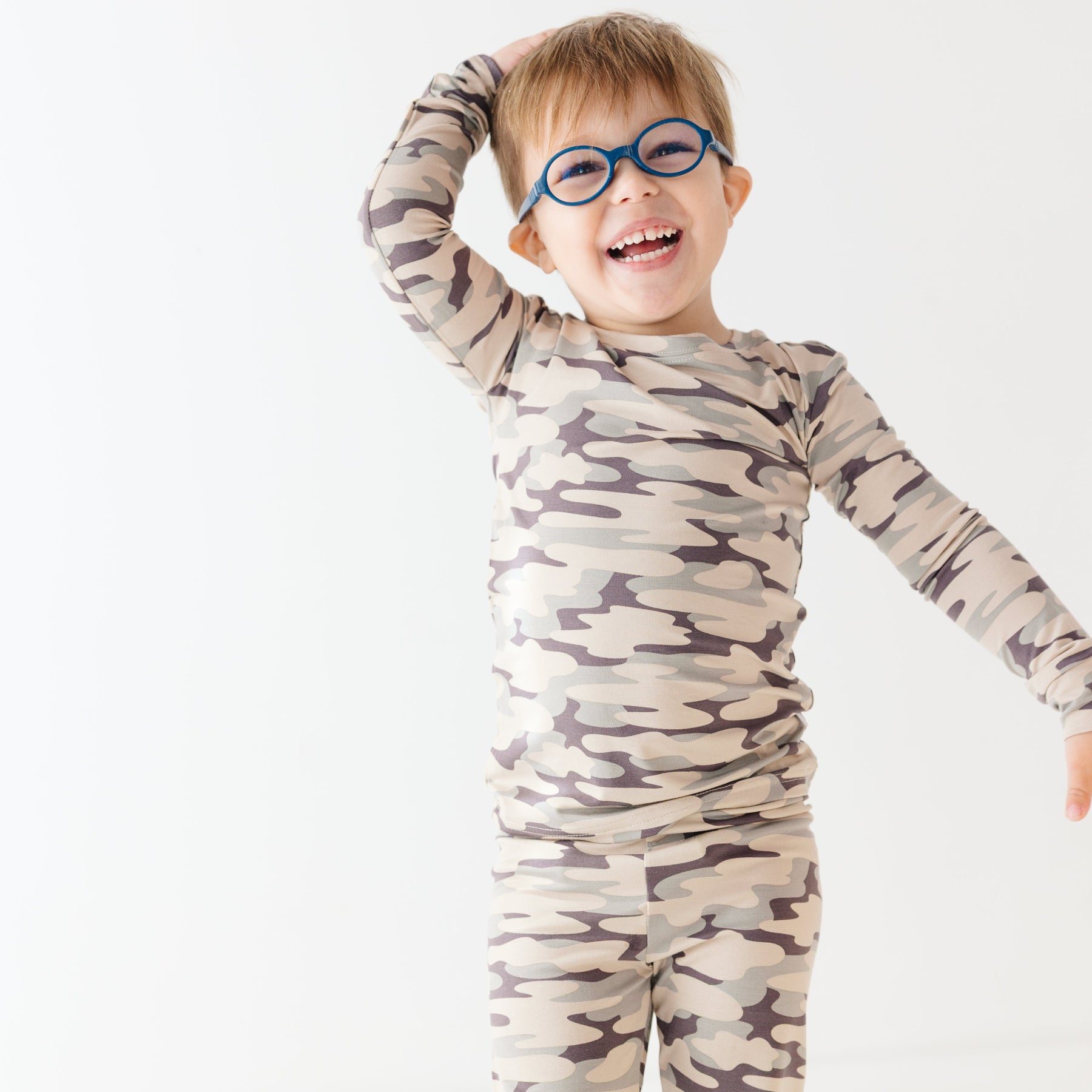 Child wearing a camouflage long sleeve pajama set on a white background