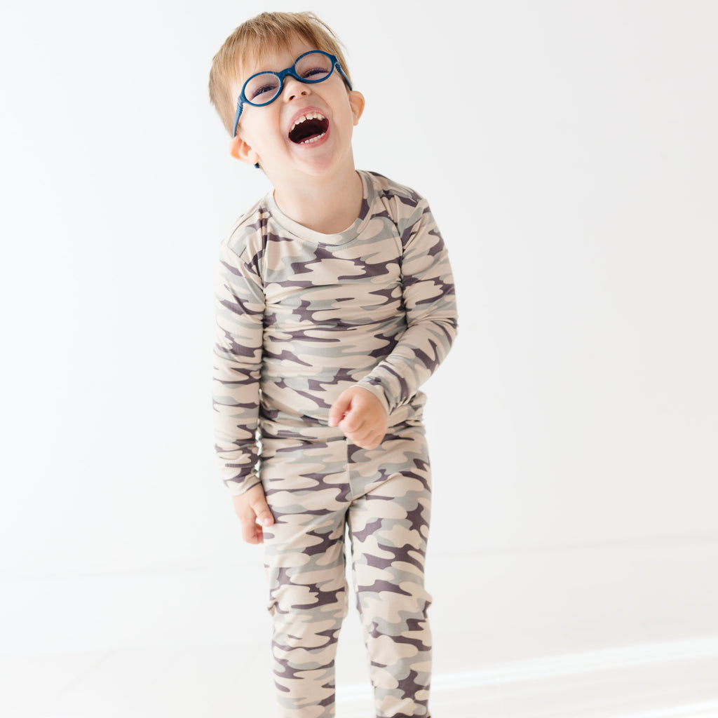 Child wearing a camouflage long sleeve pajama set on a white background