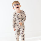 Child wearing a camouflage long sleeve pajama set on a white background