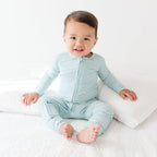 Baby wearing a light blue and white striped onesie sitting on a white surface.