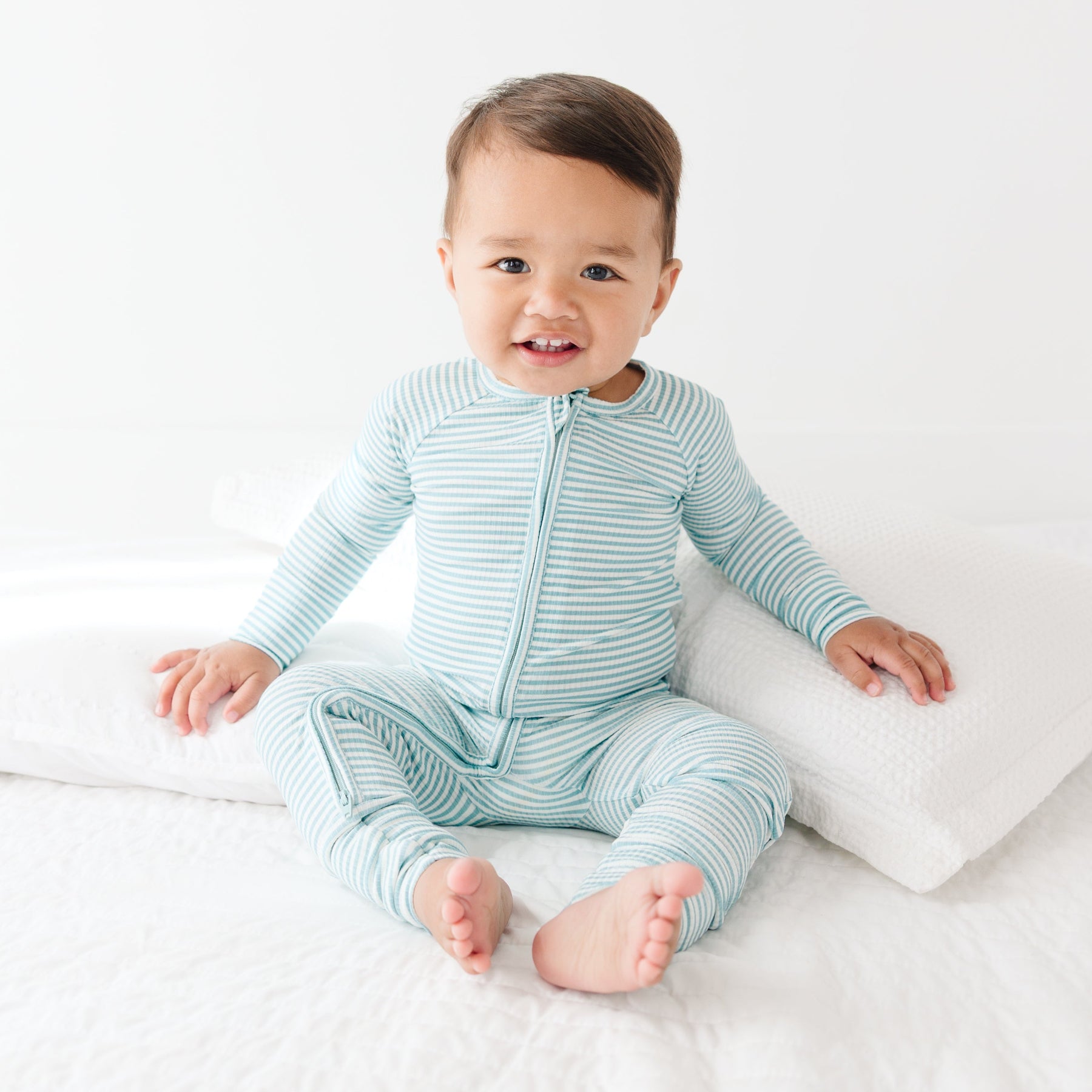 Baby wearing a light blue and white striped onesie sitting on a white surface.