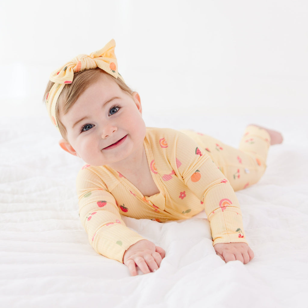 Baby wearing a yellow outfit with fruits patterns and a matching headband on a white background