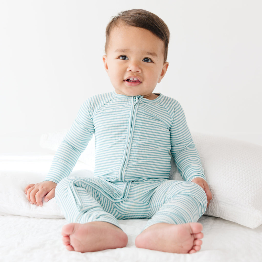 Baby wearing a light blue and white striped onesie sitting on a white surface.