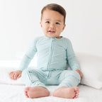 Baby wearing a light blue and white striped onesie sitting on a white surface.