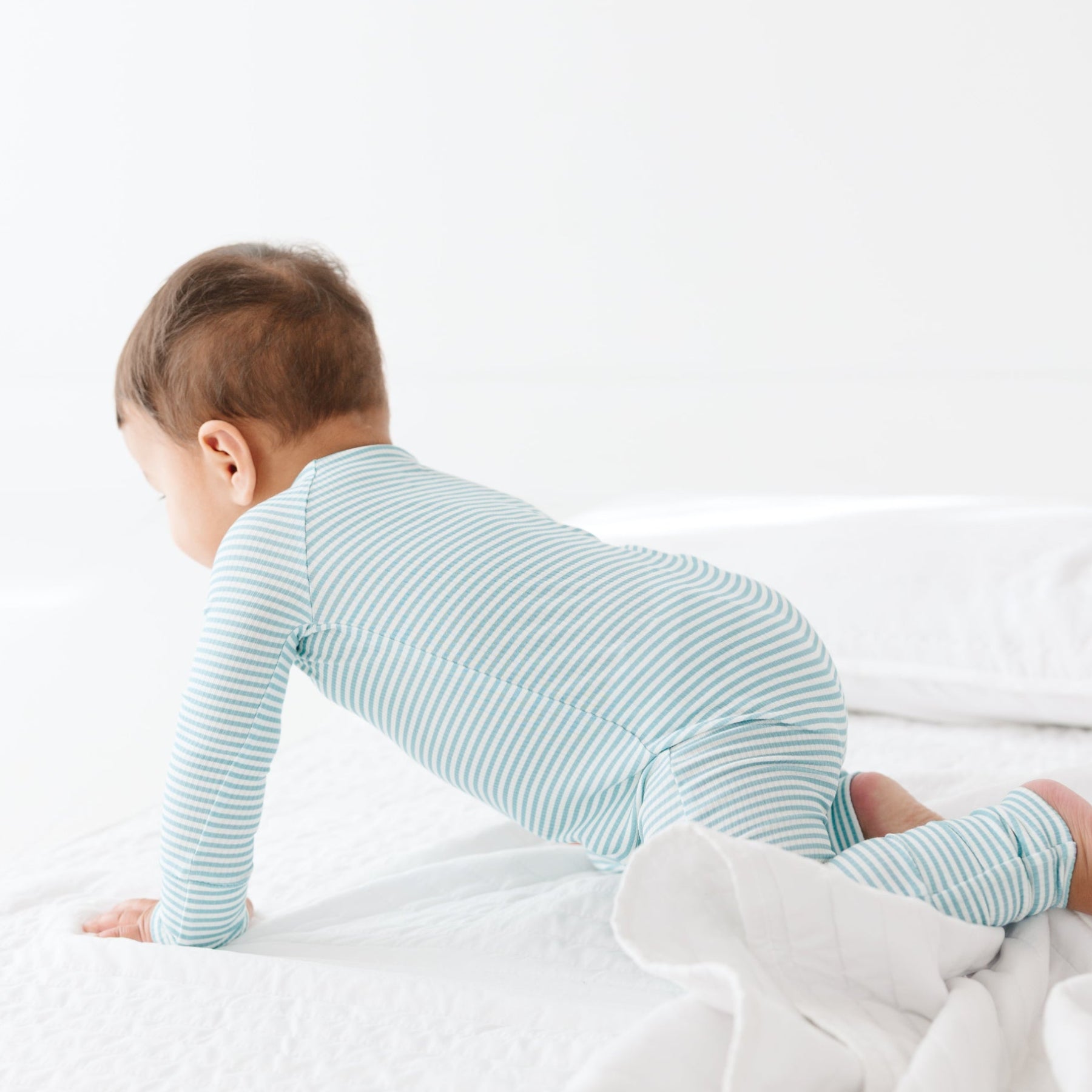 Baby wearing a light blue and white striped onesie on a plain background