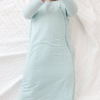 Baby lying on a white blanket wearing a light blue striped onesie and sleep sack.