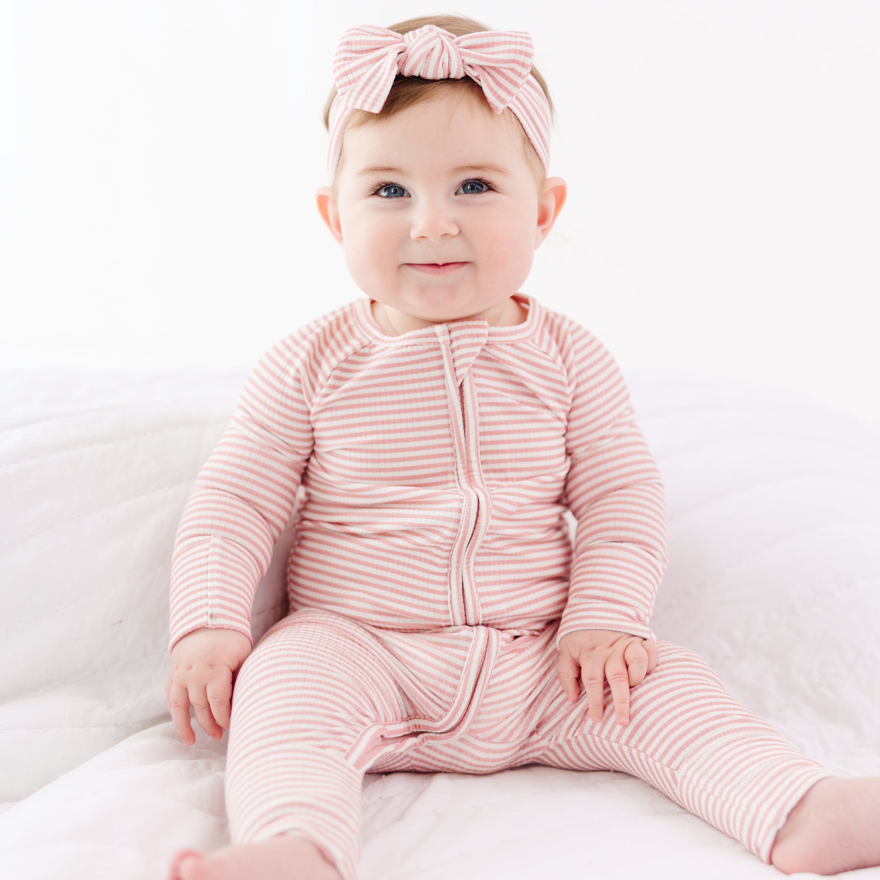 Baby wearing a pink striped outfit and headband on a white background