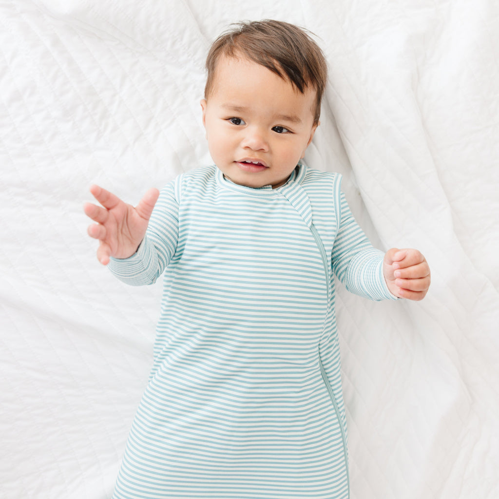 Baby wearing a light blue and white striped onesie and sleeping bag on a white background
