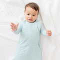 Baby wearing a light blue and white striped onesie and sleeping bag on a white background