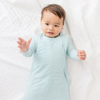 Baby wearing a light blue and white striped onesie and sleeping bag on a white background