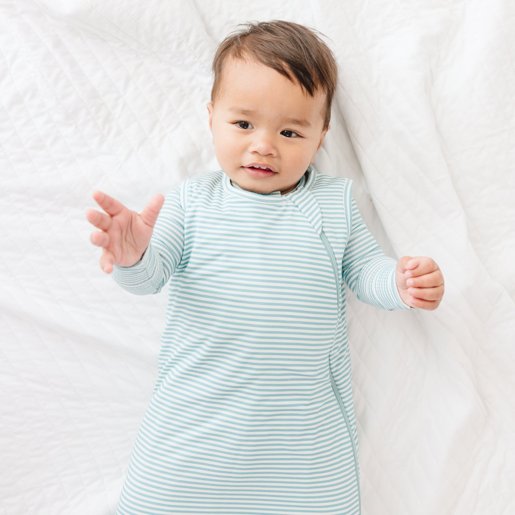 Baby wearing a light blue and white striped onesie and sleeping bag on a white background