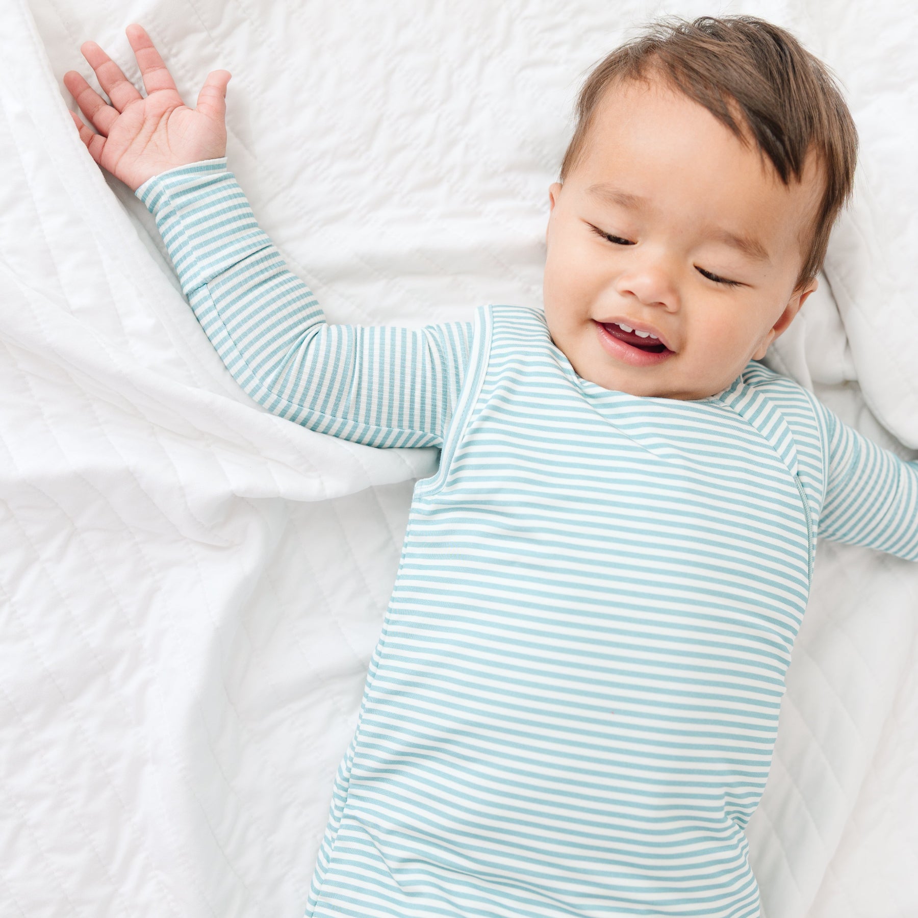 Baby wearing a light blue and white striped onesie and sleeping bag on a white background