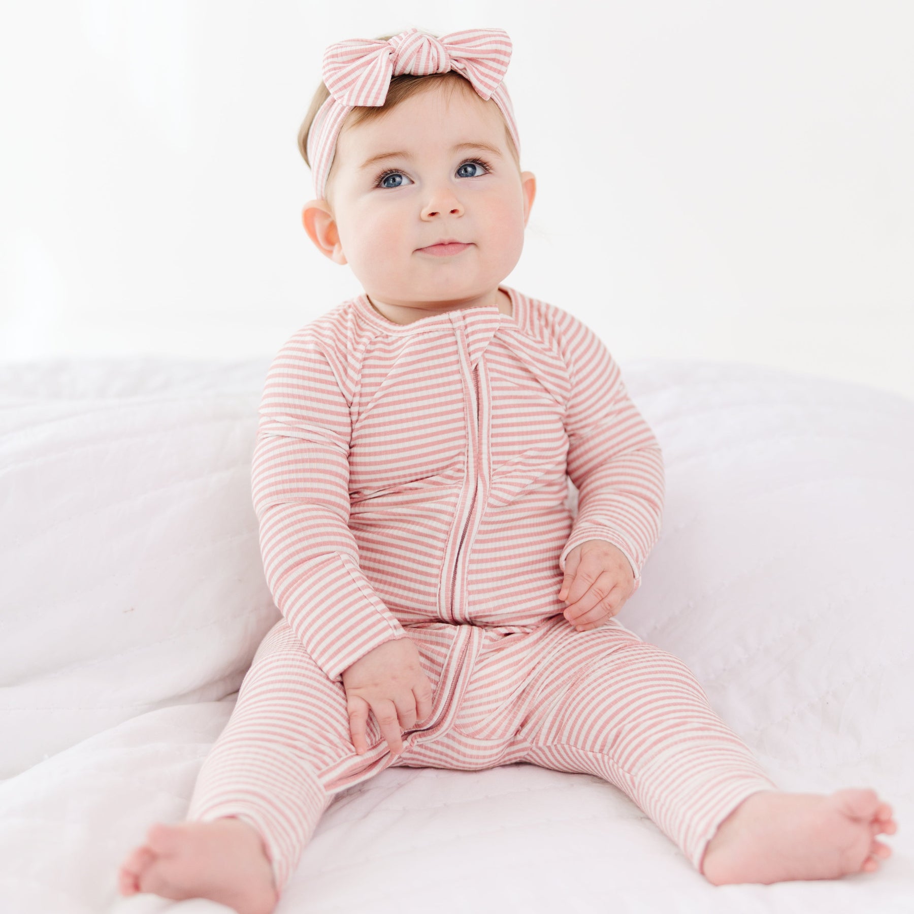 Baby wearing a pink striped outfit and headband on a white background