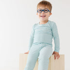 Child wearing a light blue and white striped outfit sitting on a wooden block against a white background