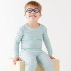 Child wearing a light blue and white striped outfit sitting on a wooden block against a white background