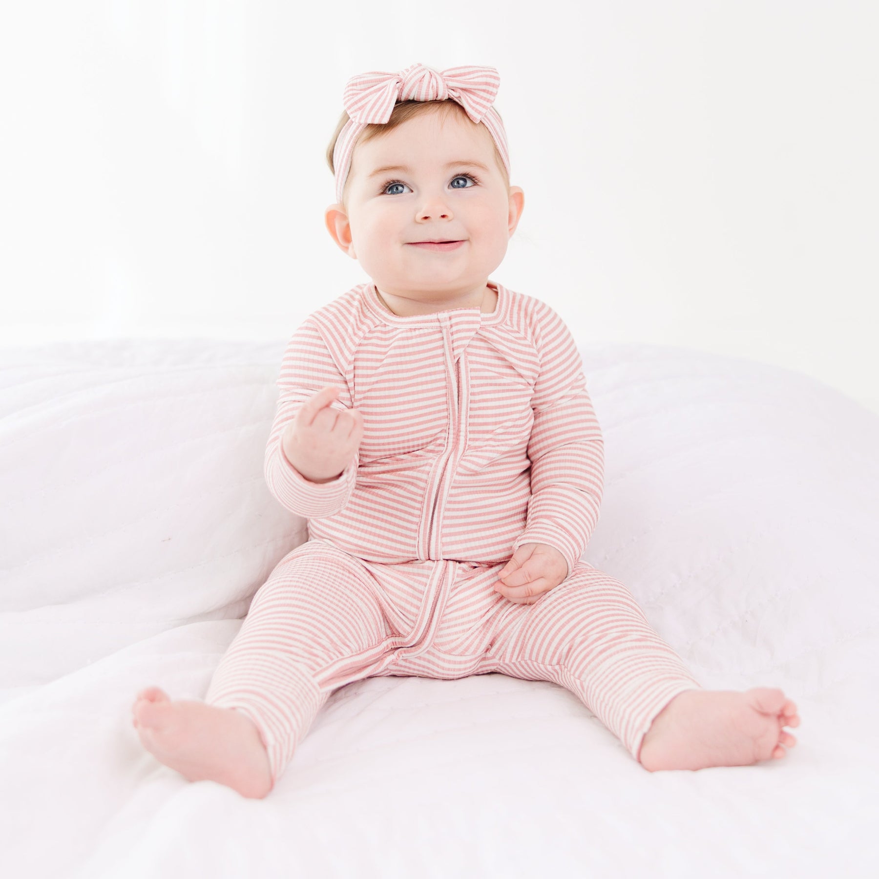 Baby wearing a pink and white striped outfit with a matching headband on a white background