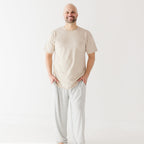 Man wearing a beige t-shirt and light gray pants on a white background