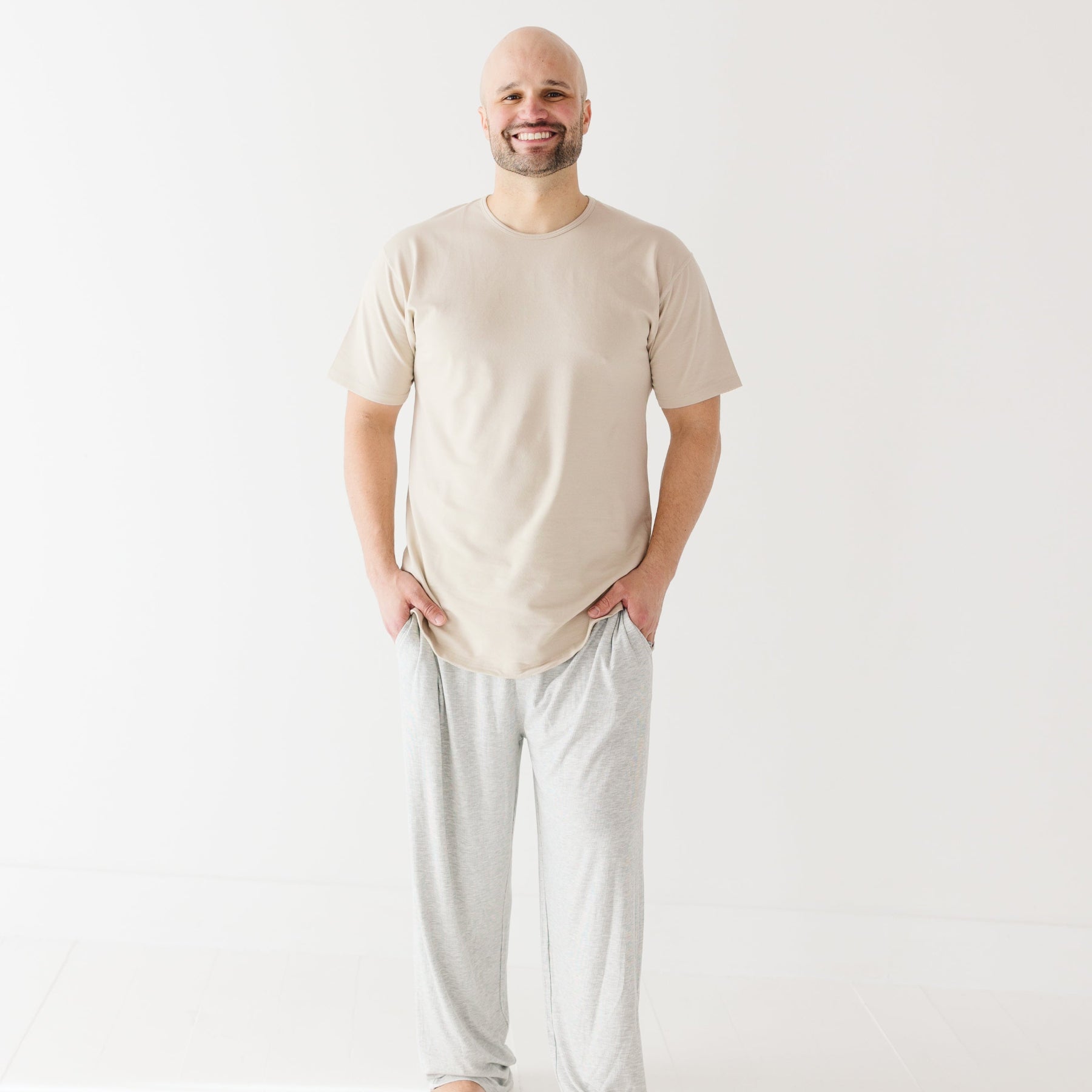 Man wearing a beige t-shirt and light gray pants on a white background