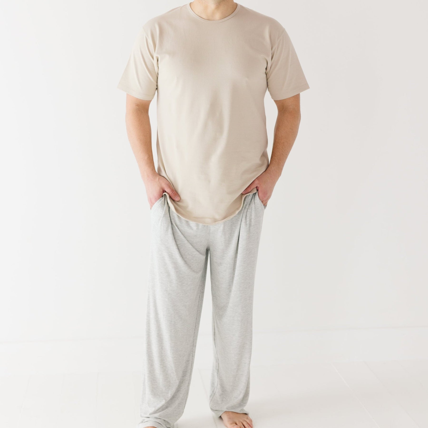 Man wearing a beige t-shirt and light gray pants on a white background