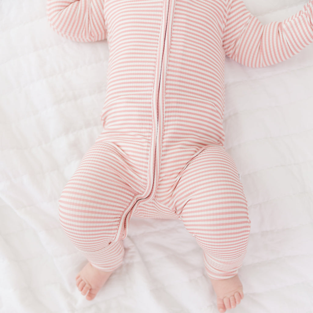 Baby in a pink striped onesie lying on a white surface