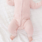 Baby in a pink striped onesie lying on a white surface