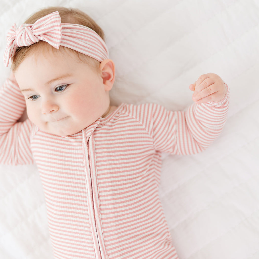 Baby wearing a pink striped outfit and headband on a white background