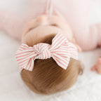Baby with a pink and white striped bow on a light background