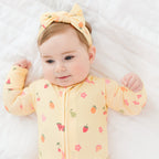 Baby wearing a yellow outfit with fruits patterns and a matching headband on a white background