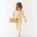 Child wearing a yellow pajama set with fruit pattern, holding a basket of fruits on a white background