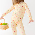 Child wearing a yellow pajama set with fruit patterns, holding a basket of fruits on a white background
