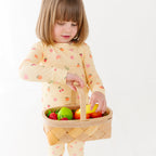 Child wearing a yellow pajama set holding a basket with fruits on a white background