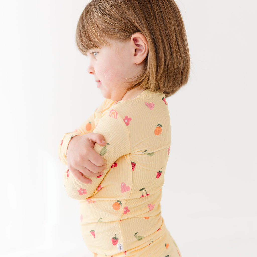 Child wearing a yellow long-sleeve shirt with fruit pattern on a white background