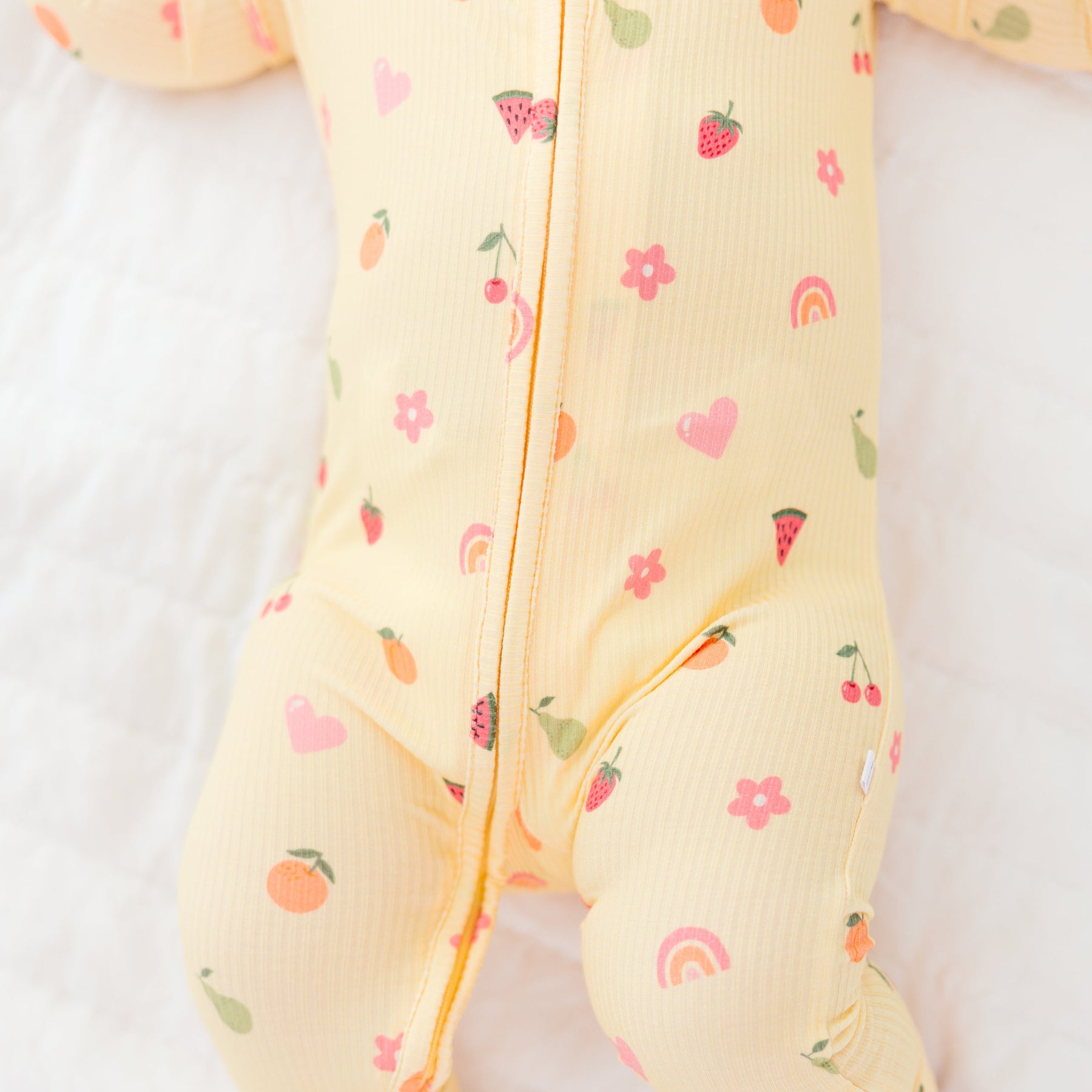 Baby wearing a yellow outfit with fruits patterns on a white background