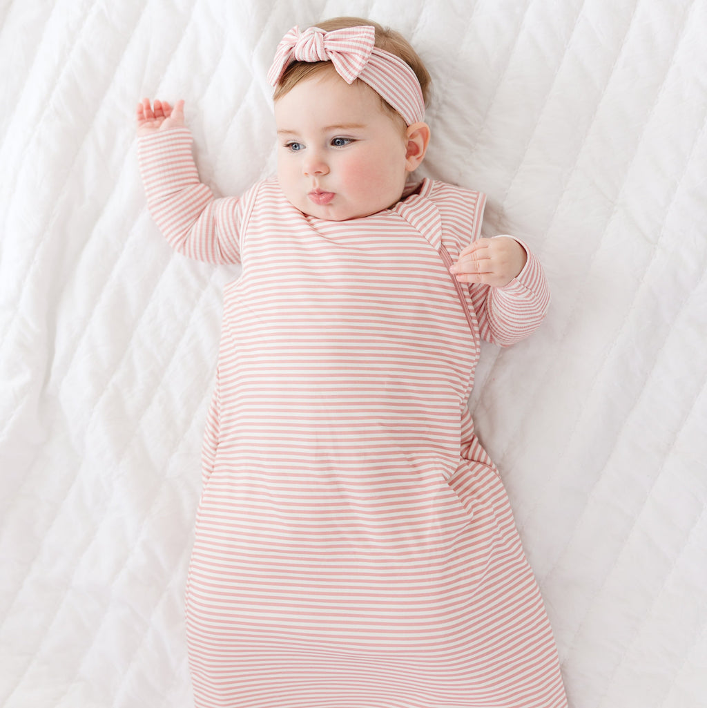 Baby wearing a pink and white striped outfit with a matching headband on a white background