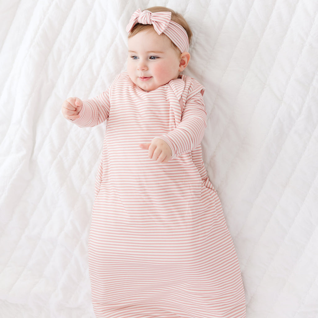 Baby in a pink striped sleeping bag and headband lying on a white blanket