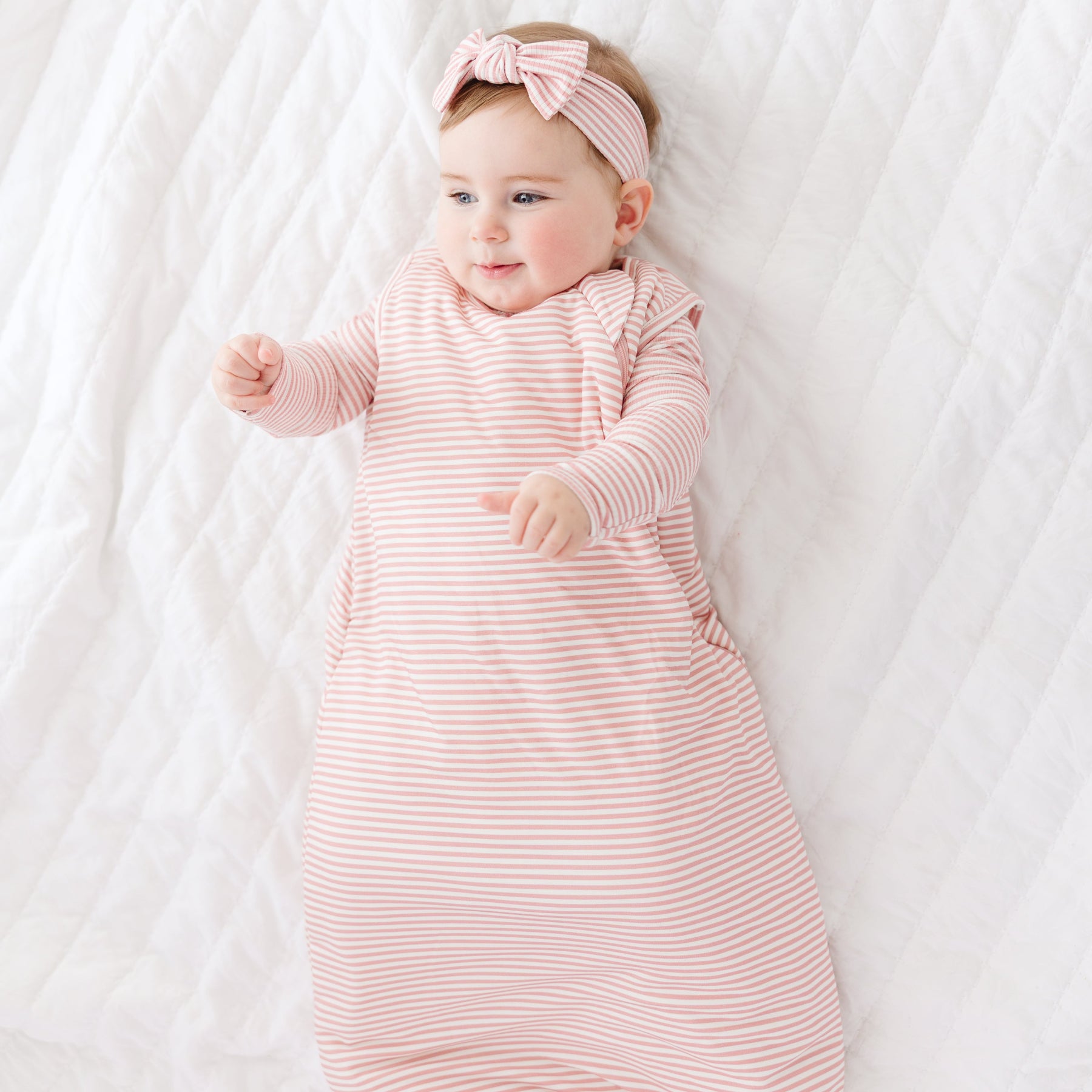 Baby in a pink striped sleeping bag and headband lying on a white blanket