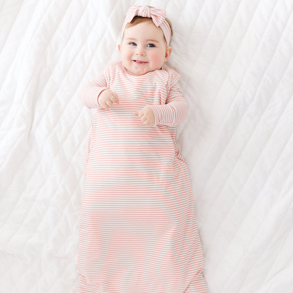 Baby in a pink striped sleeping bag and headband lying on a white blanket