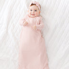 Baby in a pink striped sleeping bag and headband lying on a white blanket