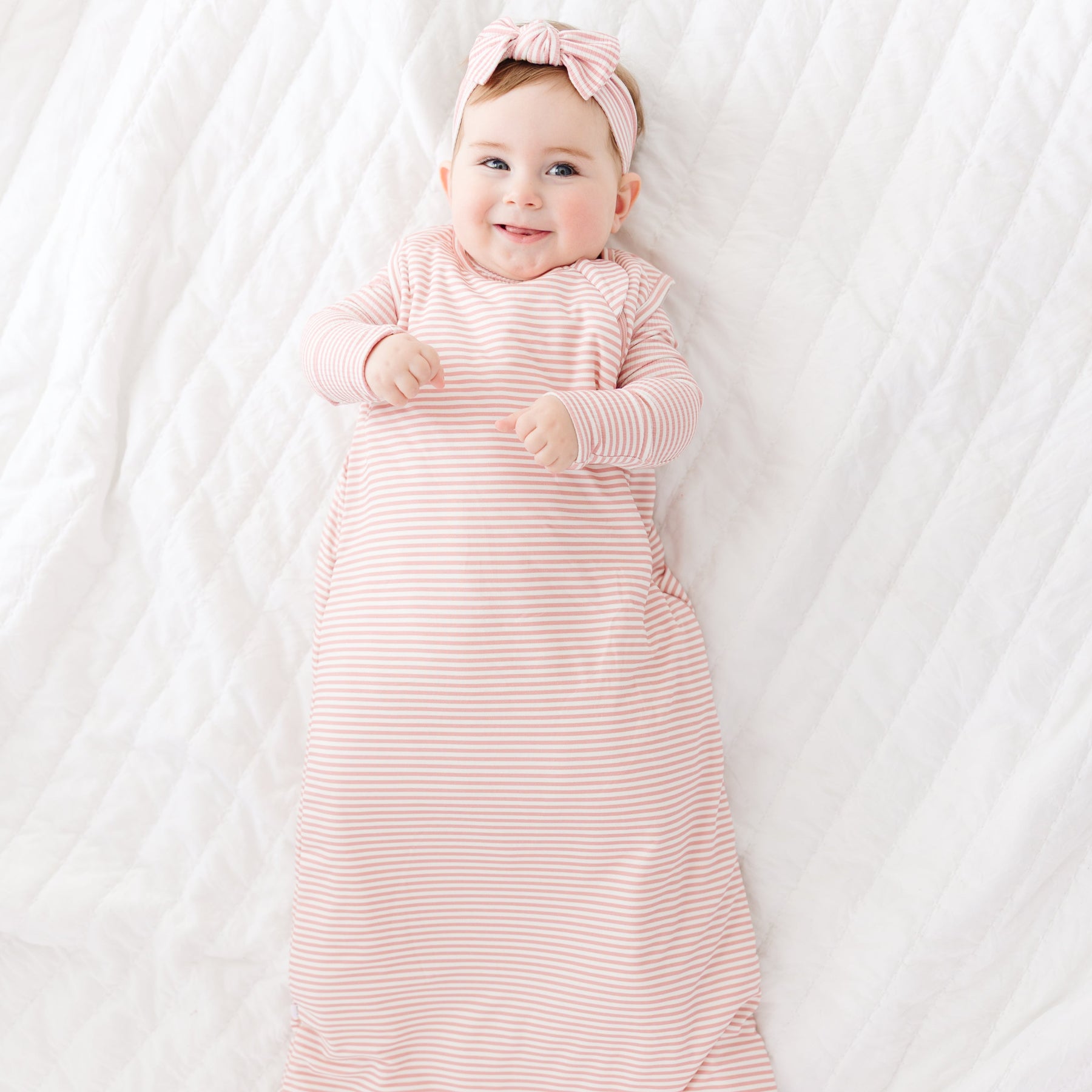 Baby in a pink striped sleeping bag and headband lying on a white blanket