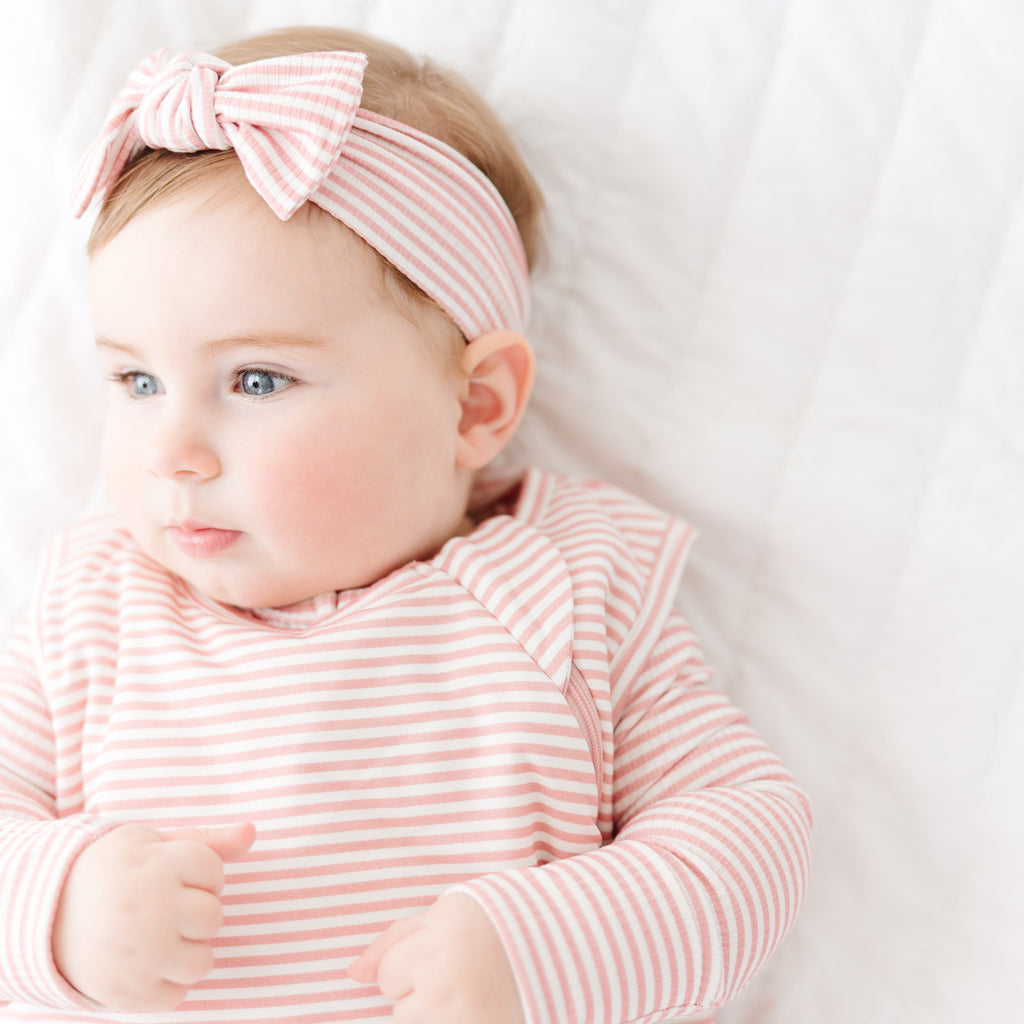 Baby wearing a pink and white striped outfit with a matching headband on a white background