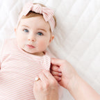 Close up of a baby in a pink striped sleeping bag and headband lying on a white blanket