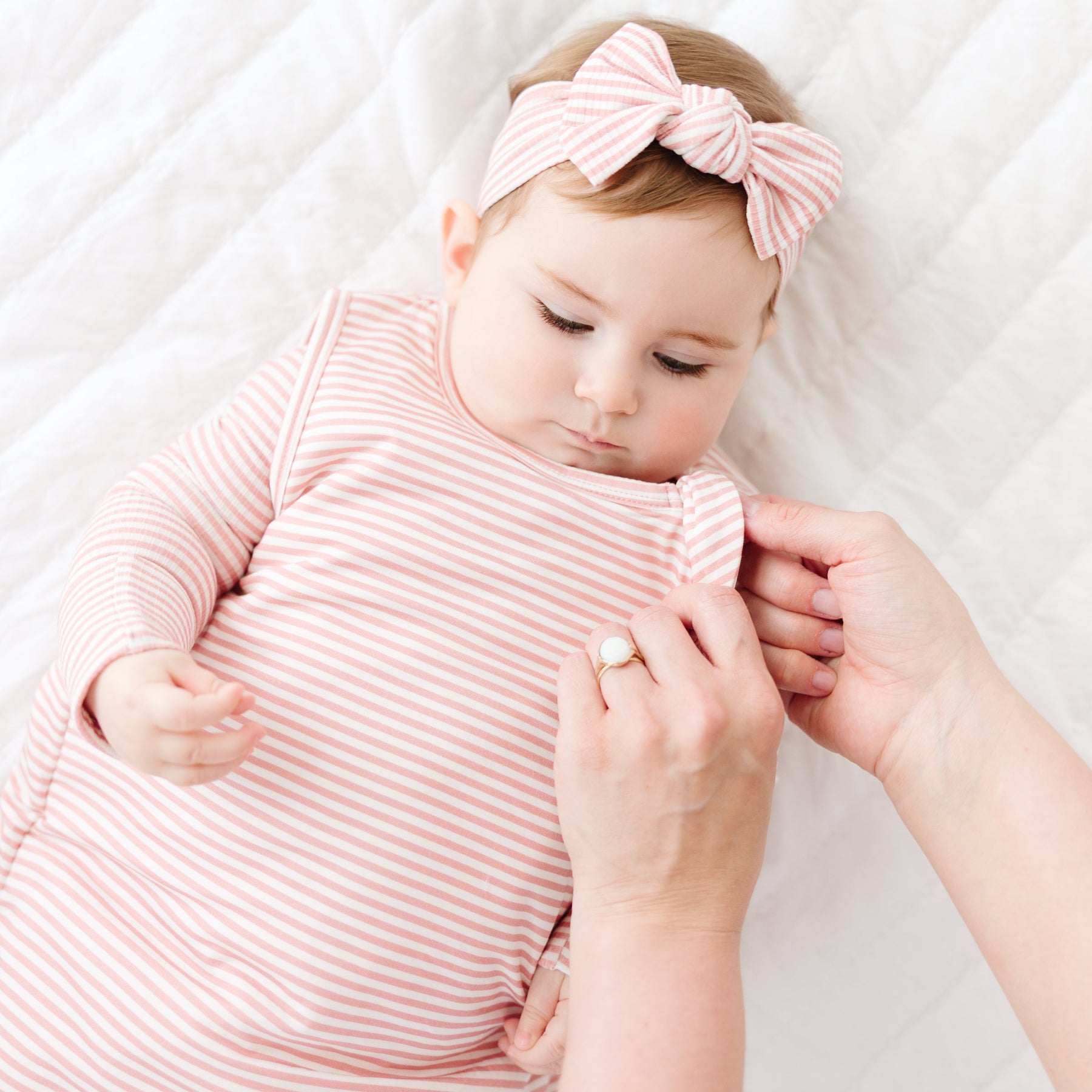 Baby in pink striped outfit with headband being held by an adult on a white background