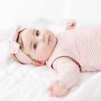 Baby in a pink striped sleeping bag and headband lying on a white blanket
