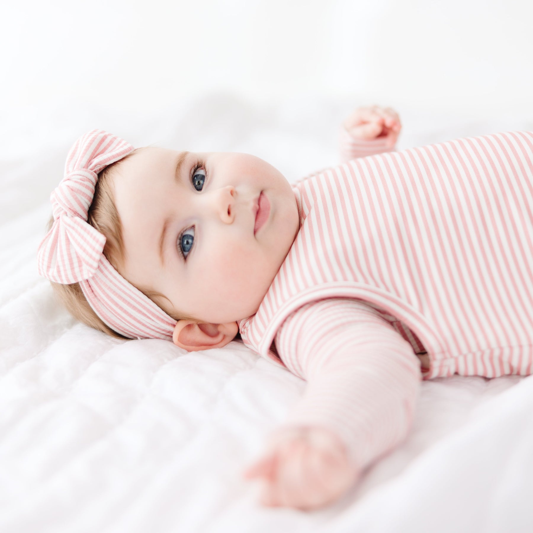 Baby in a pink striped sleeping bag and headband lying on a white blanket