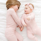 Two children in matching pink striped outfits lying on a white textured surface.