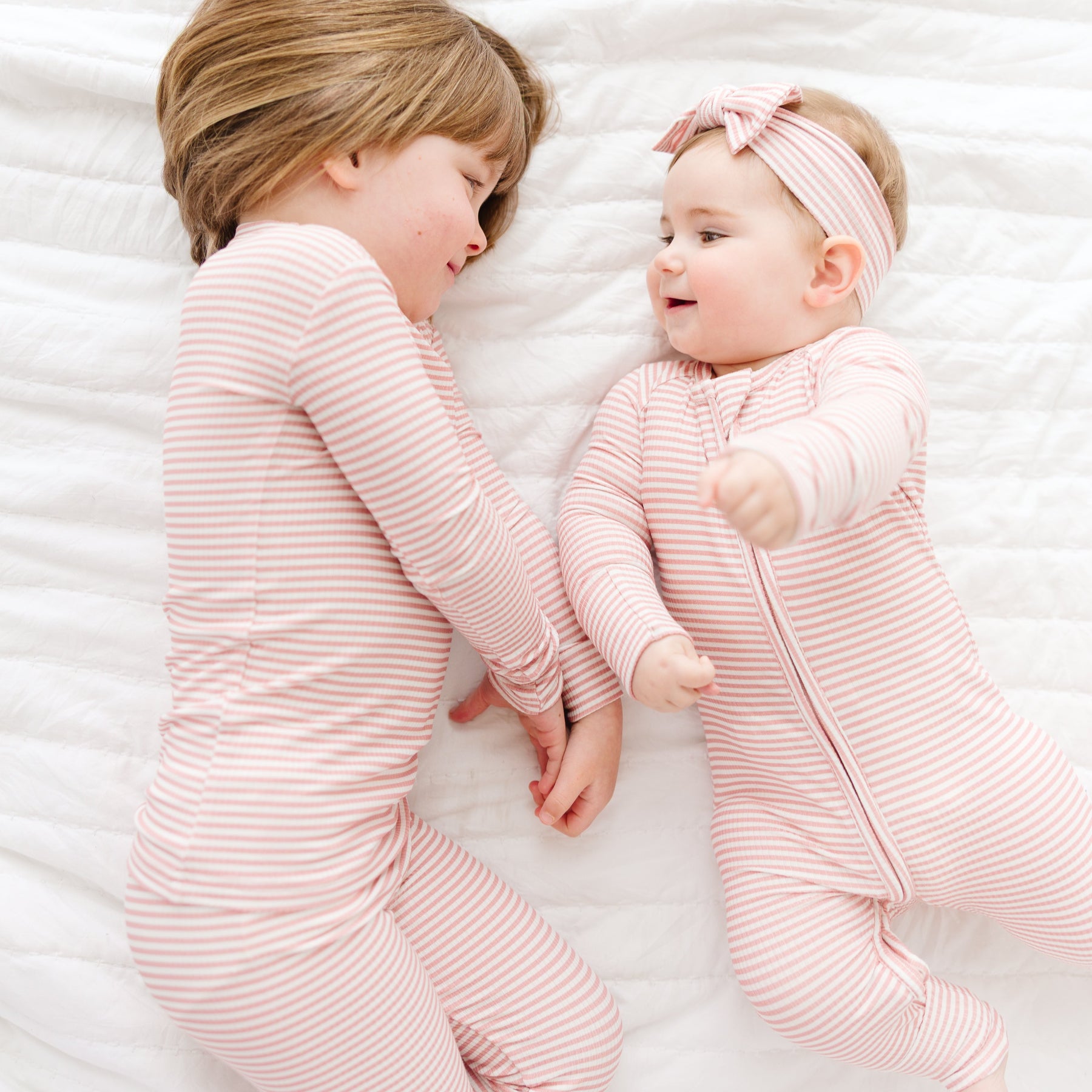 Two children in matching pink striped outfits lying on a white textured surface.