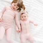 Two children in matching pink striped pajamas lying on a white textured surface.