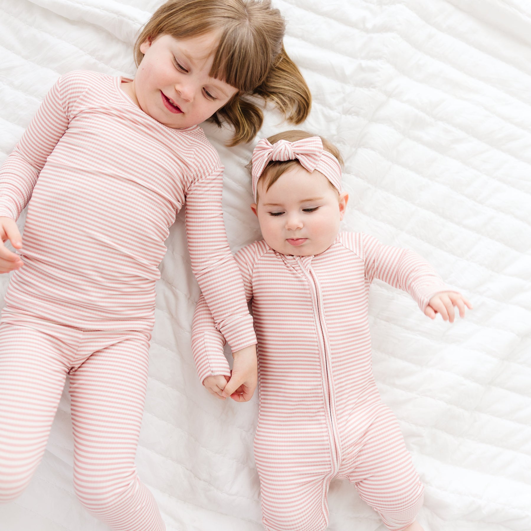 Two children in matching pink striped pajamas lying on a white textured surface.