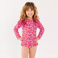 Young girl wearing a red floral swimsuit with long sleeves on a white background