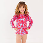 Young girl wearing a red floral swimsuit with long sleeves on a white background
